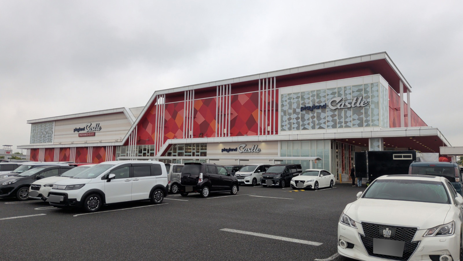 プレイランドキャッスル大垣の店舗外観。赤い菱形デザインの外壁に「playland Castle」のロゴが掲げられ、曇り空の朝、駐車場に車が停まっています。